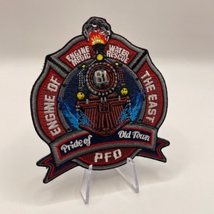 May include: Embroidered patch with a red, white, and blue design. It features a train engine with the words "Engine Medic" and "Water Rescue" on the top. The words "Engine 1 of The East" are on the left side of the patch. The words "Pride of Old Town PFD" are on the bottom of the patch.
