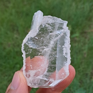 Puede incluir: Un cristal de cuarzo transparente con una textura rugosa y natural. El cristal es translúcido y tiene un ligero brillo.