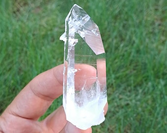 May include: A clear quartz crystal point with a double termination. The crystal is about 5 cm long and has a natural, rough texture.
