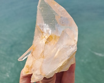 May include: A large, clear quartz crystal with a golden hue. The crystal is pointed at the top and has a rough, natural texture.