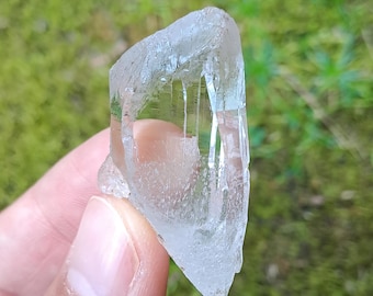 May include: A clear, faceted crystal with a pointed tip. The crystal has a natural, rough texture and appears to be translucent.