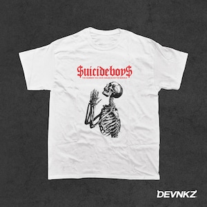 May include: White t-shirt with a black and white image of a skeleton praying. The text "Suicideboys" is printed in red above the image and the text "The number you have dialed is not in service" is printed in red below the image.