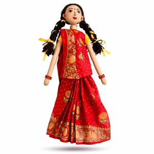Könnte beinhalten: Handgefertigte Puppe in einem traditionellen indischen Sari. Die Puppe hat schwarze Zöpfe mit gelben Bändern, einen roten und goldenen Sari und rote Armbänder. Das Gesicht der Puppe ist mit zarten Merkmalen bemalt und trägt eine kleine Perlenkette.