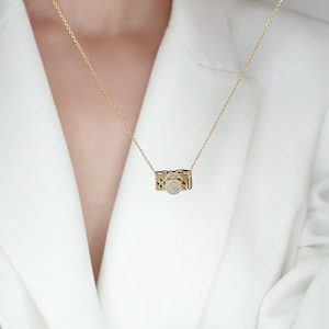 May include: A gold necklace with a camera pendant encrusted with small clear stones.