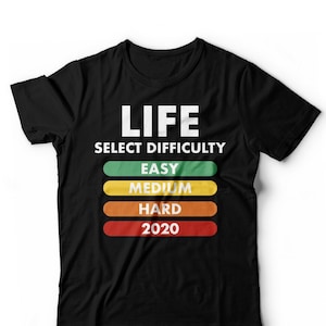 May include: Black t-shirt with white text that reads "LIFE SELECT DIFFICULTY" with a series of coloured bars below that read "EASY", "MEDIUM", "HARD", and "2020".