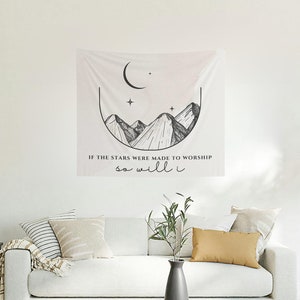 Puede incluir: Un tapiz blanco con una ilustración en blanco y negro de montañas, una luna creciente y estrellas. El texto "Si las estrellas fueron hechas para adorar, yo también lo haré" está impreso debajo de la ilustración.