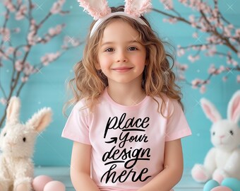 May include: A young child wearing a pink shirt with the text "place your design here" in black. The child is wearing bunny ears and sitting on a wooden floor with Easter eggs.