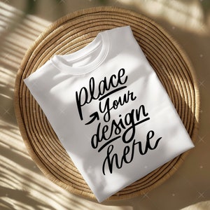Puede incluir: Camiseta blanca con el texto "place your design here" escrito en cursiva negra sobre una superficie de mimbre tejido.