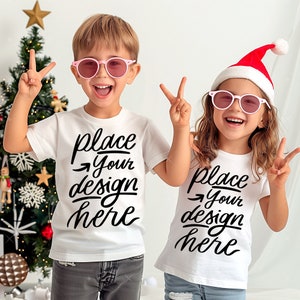 May include: Two children wearing white t-shirts with the text "place your design here" printed on them. The child on the left is wearing pink sunglasses and the child on the right is wearing a red Santa hat and pink sunglasses.