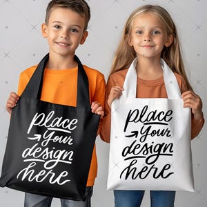 May include: Two children holding tote bags. One bag is black with white text that reads "place your design here." The other bag is white with the same text. Both children are wearing long-sleeved shirts.