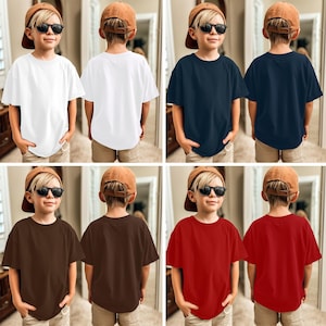 以下が含まれることがあります： 白、ネイビーブルー、ブラウン、赤の子供用Tシャツのコレクション。 各シャツは、クラシックなクルーネックと半袖です。 サングラスと野球帽をかぶった若い人がシャツを着ています。