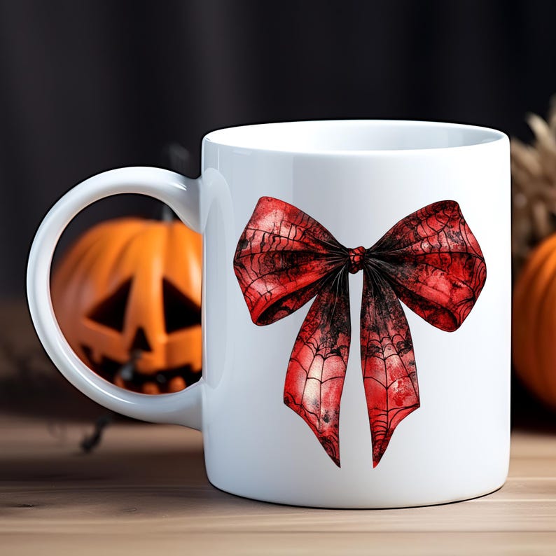 May include: White ceramic mug featuring a large red bow with a spiderweb design. The bow has a gradient effect, transitioning from red to black. The mug is set against a blurred background with a carved pumpkin, suggesting a Halloween theme.
