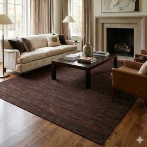 May include: A living room with a cream-colored sofa, brown rug, and a dark wood coffee table. Two brown leather armchairs sit near the fireplace. The room has large windows with beige curtains and a chandelier.