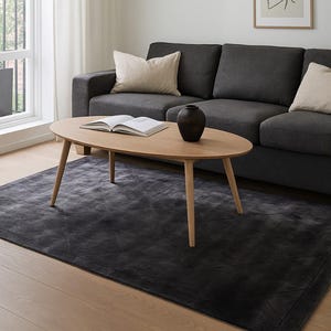 Könnte beinhalten: Ein modernes Wohnzimmer mit einem dunkelgrauen Sofa, einem ovalen Couchtisch aus hellem Holz und einem dunkelgrauen Teppich. Über dem Couchtisch, auf dem ein Buch und eine schwarze Vase stehen, hängt eine weiße Pendelleuchte. Ein gerahmtes abstraktes Kunstwerk hängt an der Wand.