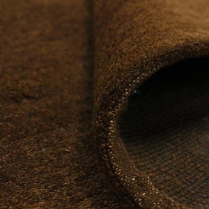 May include: Close-up of a rolled-up brown rug. The rug has a textured surface with visible fibers and a rolled edge. The color is a rich, warm brown, with a hint of lighter flecks along the edge. The rug appears to be made of a thick, durable material.