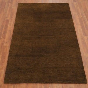 May include: A rectangular, brown rug with a textured surface. The rug is placed on a wooden floor. The rug's color is a deep, earthy brown, suitable for living rooms or bedrooms.