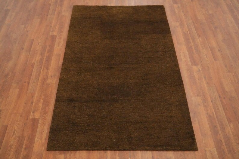May include: A rectangular, brown rug with a textured surface. The rug is placed on a wooden floor. The rug's color is a deep, earthy brown, suitable for living rooms or bedrooms.