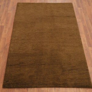 May include: A rectangular brown rug with a textured surface. The rug is placed on a wooden floor with a warm, reddish-brown tone. The rug's color is a solid, earthy brown.