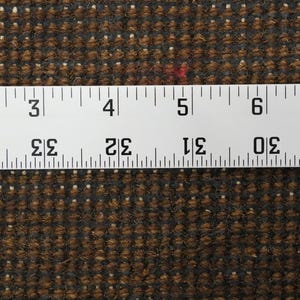 May include: Close-up of a brown and black textured fabric with a white ruler across the top. The ruler shows measurements from 29 to 34 inches. The fabric has small white and red flecks.