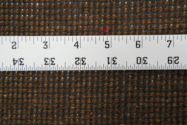 May include: Close-up of a brown and black textured fabric with a white ruler across the top. The ruler shows measurements from 29 to 34 inches. The fabric has small white and red flecks.