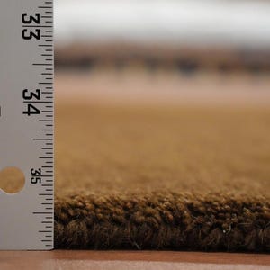 May include: Close-up of a brown rug with a ruler showing the pile height. The rug has a dark brown edge and a lighter brown surface. The ruler indicates the rug is approximately 33 inches long.