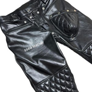 May include: Black leather trousers featuring quilted diamond pattern details on the knees and a quilted pouch. The trousers have multiple silver snap closures and a zip. The text "ssea leather" is visible.