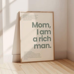Könnte beinhalten: Ein gerahmter Druck mit beigefarbenem Hintergrund und einem grünen Textüberlagerung, der "Mama, ich bin ein reicher Mann" lautet. Der Text ist in fetter, serifenloser Schrift. Der Druck ist von einem dünnen Holzrahmen umgeben.
