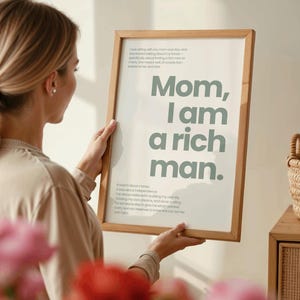 Könnte beinhalten: Ein gerahmter Druck mit einem hellgrünen Hintergrund und dem Text "Mama, ich bin ein reicher Mann." Der Druck wird von einer Person vor einer weißen Wand gehalten.
