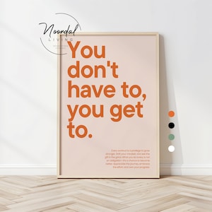 Puede incluir: Un cartel enmarcado con el texto "You don't have to, you get to." en letras naranjas sobre un fondo melocotón. El cartel también incluye texto más pequeño en la parte inferior. El marco es de color madera clara. El logotipo de Noordal Living está en la parte superior.