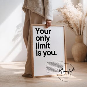 Könnte beinhalten: Ein gerahmter Druck mit dem Text "Your only limit is you." in minimalistischem Stil. Der Druck wird von einer Person gehalten. Der Rahmen besteht aus hellem Holz. Der Hintergrund umfasst eine Vase mit getrockneten Pflanzen.