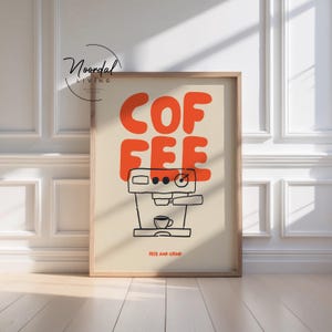 May include: A framed wall art print featuring a light beige background with the word COFFEE in large, bold orange letters. Below the text is a black line drawing of an espresso machine with a small cup, and the text RISE AND GRIND in orange.