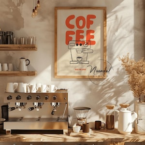 May include: A framed poster with the word "COFFEE" in orange block letters above a black and white illustration of an espresso machine. A stainless steel espresso machine and coffee-making accessories are in the foreground.