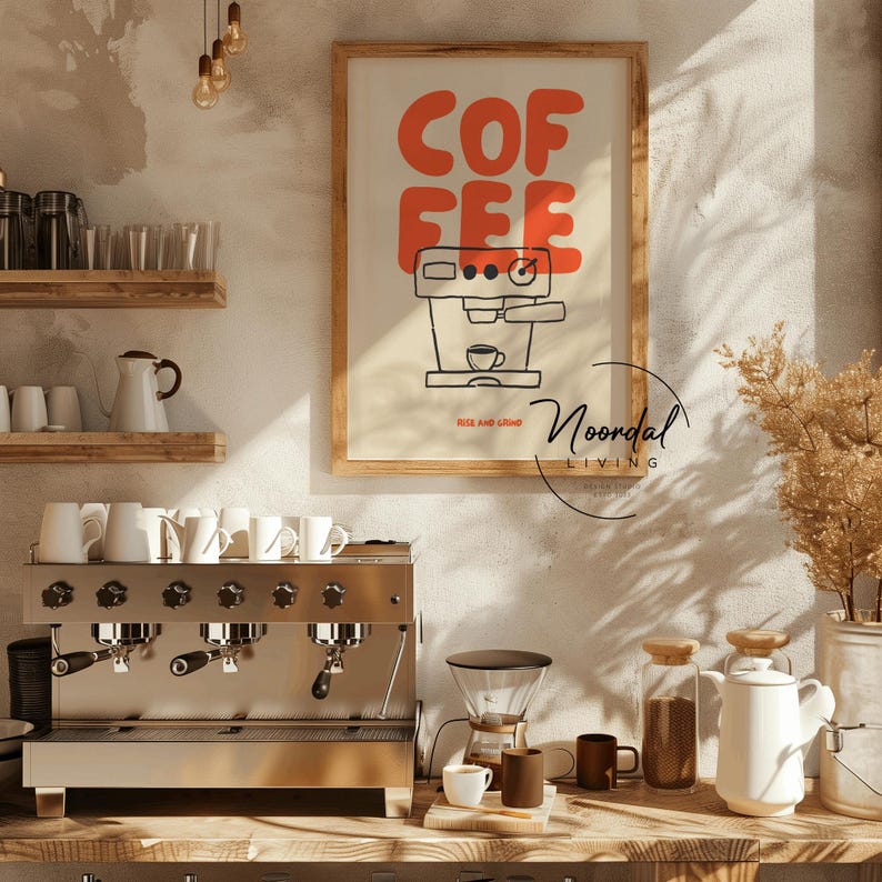 May include: A framed poster with the word "COFFEE" in orange block letters above a black and white illustration of an espresso machine. A stainless steel espresso machine and coffee-making accessories are in the foreground.