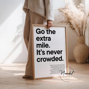 Könnte beinhalten: Ein rechteckiges gerahmtes Wandbild mit einem hellen Holzrahmen. Der weiße Druck zeigt den schwarzen Text: Go the extra mile. It’s never crowded. Darunter befindet sich kleinerer schwarzer Text: Whether it’s in your career, your craft, or your personal growth.