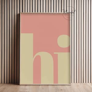 May include: A framed art print with a minimalist design. The artwork features the word "hi" in a soft yellow font against a pink background. The print is in a wooden frame and is displayed against a wood-paneled wall.