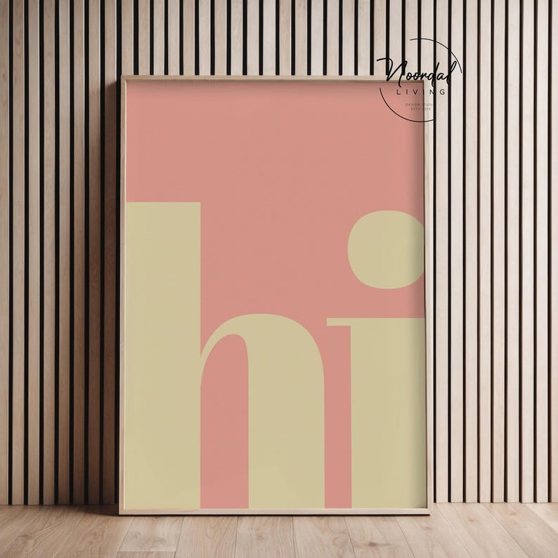 May include: A framed art print with a minimalist design. The artwork features the word "hi" in a soft yellow font against a pink background. The print is in a wooden frame and is displayed against a wood-paneled wall.