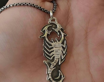 May include: A silver scorpion pendant necklace with a detailed design. The scorpion is facing to the right and has a textured surface.