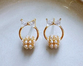 May include: A pair of gold earrings with a small pearl sphere and a clear rhinestone bow on each earring.