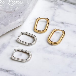 Peut inclure: Deux paires de créoles rectangulaires, une paire en or et une paire en argent. Les boucles d'oreilles sont sur une surface en marbre blanc. La Lune Accessory est écrit en noir sur la surface.