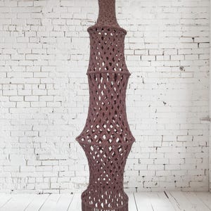 Op de afbeelding: Een grote, bruine macramé hanglamp met een franje onderkant. De lamp is gemaakt van dik touw en heeft een geometrisch ontwerp.