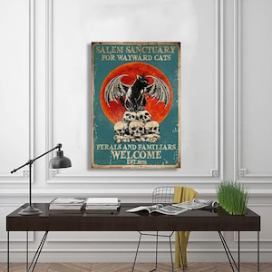 Könnte beinhalten: Ein Vintage-Poster mit einer schwarzen Katze mit Flügeln, die auf einem Schädelhaufen sitzt. Das Poster hat einen roten Mond und einen blauen Hintergrund mit dem Text "Salem Sanctuary for Wayward Cats" und "Ferals and Familiars Welcome Est. 1692".