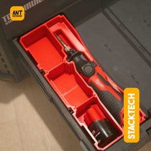 Puede incluir: Un soldador Milwaukee rojo y negro con una batería, almacenado en una bandeja organizadora de plástico rojo. La bandeja está dentro de una caja de herramientas negra con la palabra "STACKTECH" impresa en el lateral.