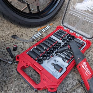 Puede incluir: Un juego de vasos rojo y negro con una variedad de tamaños, incluyendo 10 mm, 12 mm, 14 mm, 17 mm y 19 mm. El juego está abierto y los vasos son visibles. También se puede ver un destornillador de impacto inalámbrico negro y rojo en la imagen. El juego está sobre una superficie de hormigón gris.