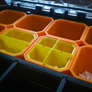 Puede incluir: Primer plano de una caja de aparejos de pesca negra y naranja con múltiples compartimentos. Los compartimentos están divididos en secciones más pequeñas con divisores amarillos.