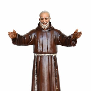 Puede incluir: Una estatua marrón de San Francisco de Asís con barba blanca y túnica marrón. Está de pie con los brazos extendidos, llevando un rosario y un cinturón de cuerda.