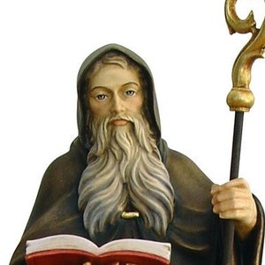 Op de afbeelding: Een houten beeld van een heilige die een boek en een staf vasthoudt. De heilige draagt een bruine robe en heeft een lange witte baard. Het beeld is geschilderd in tinten bruin, goud en wit.