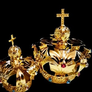 Könnte beinhalten: Zwei goldene Kronen mit Juwelenbesatz. Die größere Krone hat ein Kreuz oben und die kleinere Krone ein Kreuz an der Seite.