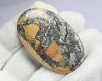 May include: A polished oval cabochon of ocean jasper with a swirling pattern of black, white, brown, and orange.