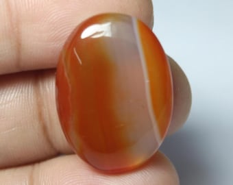 May include: A smooth, oval-shaped carnelian gemstone with orange and white banding. The stone is polished and has a glossy finish.