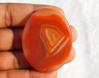 May include: Oval shaped red agate cabochon with white and orange banding. The agate has a natural, polished finish.